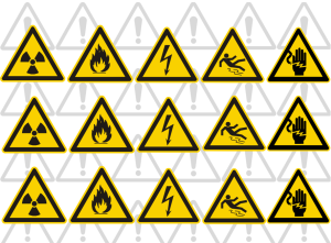 Una imagen que muestra una serie de señalizaciones de seguridad en triángulos amarillos con bordes negros, incluyendo advertencias de radiación, fuego, electricidad, resbalones y riesgos eléctricos, dispuestas en un patrón sobre un fondo con siluetas de triángulos grises.