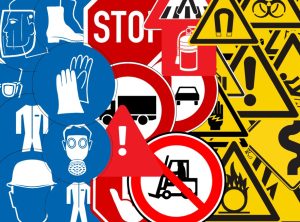Una imagen colorida que muestra una variedad de señalizaciones de seguridad, incluyendo íconos de equipo de protección personal como cascos, guantes, gafas y trajes, junto con señales de tráfico como "STOP", advertencias de peligro, prohibiciones de vehículos y símbolos de riesgo como fuego y productos químicos.