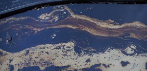 Cuerpo de agua contaminado por un derrame de petróleo, con manchas aceitosas iridiscentes y espuma en la superficie.